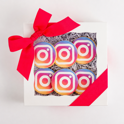 Gift box with colorful cookies shaped like Instagram logos and a red ribbon on a white background
