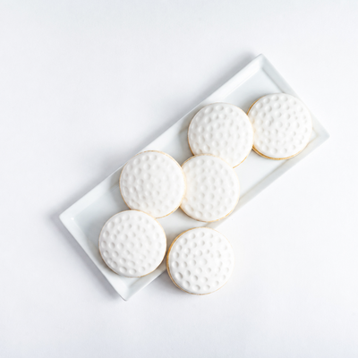 Decorative cookies shaped like golf balls on a white plate with a white background