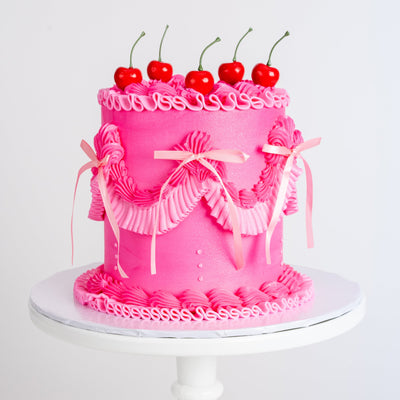 Pink Vintage Coquette cake with cherry decorations on a white stand 