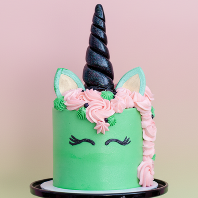 Unicorn-themed cake with a black horn, pink flowers, and green body on a gradient background