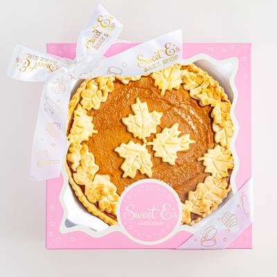 pumpkin pie with white frosting in a pink box on a light gray background